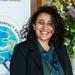 Dr Mona Ibrahim has shoulder-length curly black hair. She is smiling broadly, wearing a dark green blouse and black blazer.