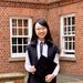 Yiwei Zhou stands in a courtyard wearing academic dress. She is smiling, holding a mortar board.