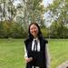 Christina Wang wears academic dress and is standing in front of a patch of grass. 