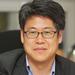 kim won sub has short black hair, wearing glasses with a grey jack with blue shirt smiling at the camera