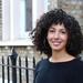 Rana Khazbak has curly black hair, wearing a black top with big silver hoop earrings smiling at the camera.