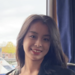 Yaxin has long dark hair. She is standing in front of a window and smiling. 