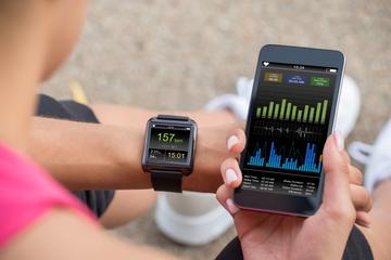 A runner wearing a smartwatch tracking their fitness statistics. They are holding their smartphone next to their wrist, looking at more detail on a fitness app.