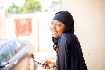 A young smiling Nigerian woman looking at the camera, holding a mobile phone