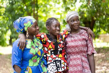 Three adolescent girls in colourful outfits. The girl in the middle has her arms around the shoulders of her friends either side. Credit: stock.adobe.com / Riccardo Niels Mayer