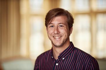 Dirk Witteveen has red hair short hair, wearing a black and red striped shirt smiling at the camera.