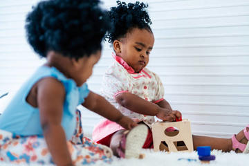 Two infant girls playing together with a shape fitter 
