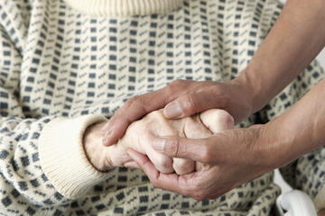 A close-up of a care worker patting an older man's hand.