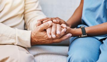 A close-up image of a nurse and a patient holding hands. 