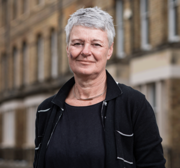 Jane barlow is wearing a black top and jacket, with short gray hair, smiling for the camera.