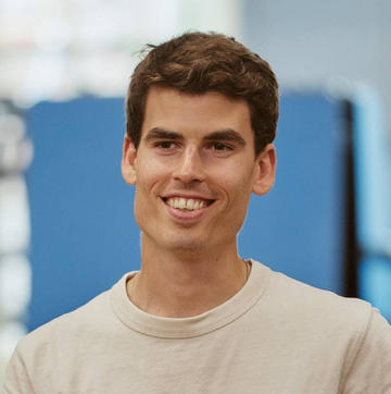 Alejandro has short brown hair, wearing a white t-shirt and smiling at the camera.