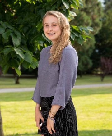 Charlotte Evans is wearing a purple top , standing sideways at the camera, with shoulder length blonde hair smiling at the camera.