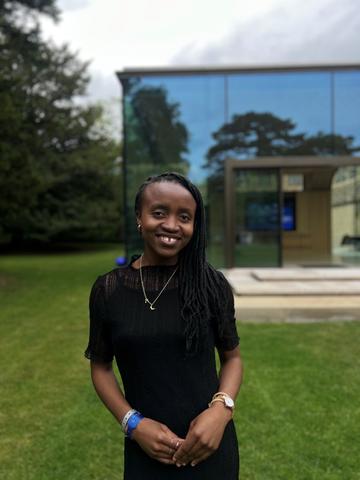 Diana mwala has shoulder length black braids, wearing a black dress smiling at the camera directly.