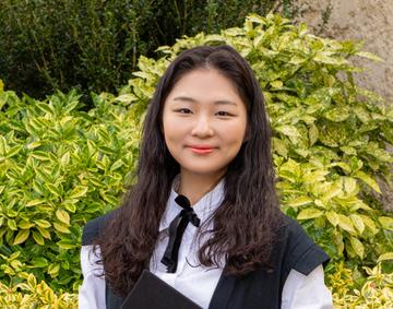 Jinseo kim Jinseo Kim is wearing graduation gown, with dark shoulder length hair smiling at the camera.
