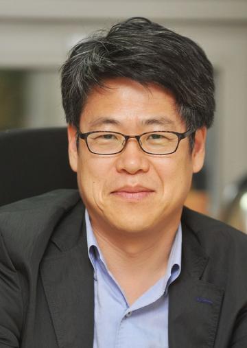 kim won sub has short black hair, wearing glasses with a grey jack with blue shirt smiling at the camera
