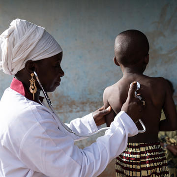A nurse in a white uniform pressing a stethoscope to the back of a young child's back. Credit: Riccardo Niels Mayer - stock.adobe.com