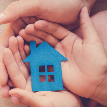 Adult and child hands holding blue paper house for family home