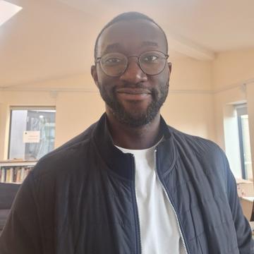 Benjamin Hornsby Odo has short afro hair, wearing round shaped glasses, with a dark  blue and white t-shirt smiling at the camera.