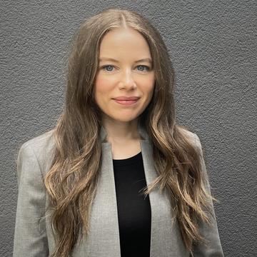 Cherise Regier has long brown hair and is wearing a grey suit, smiling gently at the camera