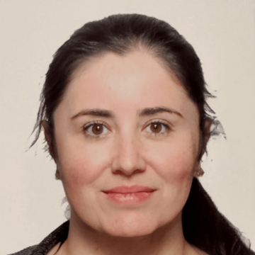 Gabriela de Carvalho has dark brown hair tied back - she has hazel eyes and is wearing a grey jumper.