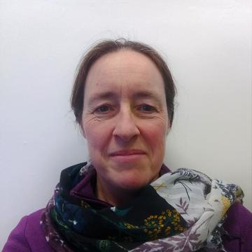 katharine de villiers is wearing a scarf with a purple top and smiling gently as she looks at the camera.