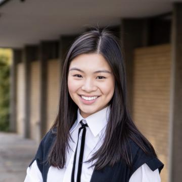 Margaret lim is wearing a graduation gown with black shoulder length hair, smiling at the camera.