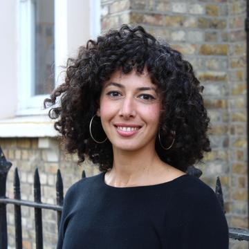Rana khazbak Rana Khazbak has curly black hair, wearing a black top with big silver hoop earrings smiling at the camera.