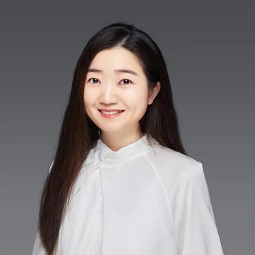 Zuyi Fang is smiling at the camera, she has long hair past her shoulders and is wearing a white top.