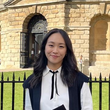 Wearing a graduation gown, Chloe stands in front of a University of Oxford building.