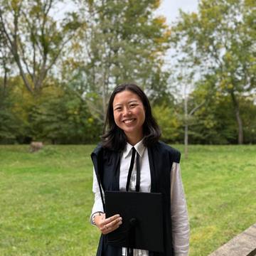Christina Wang wears academic dress and is standing in front of a patch of grass. 