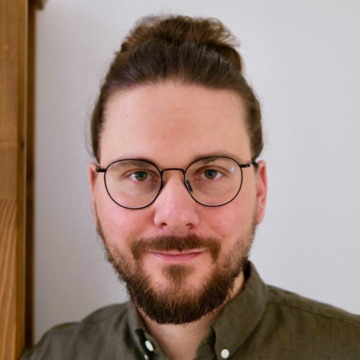 Dr Jan Helmdag has short dark hair, is wearing a brown shirt with glasses, smiling at the camera