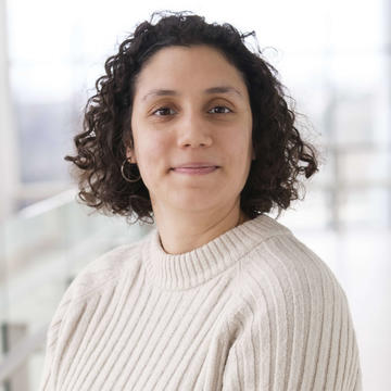 Dr Elifcan Celebi has cropped brown hair and is wearing a beige jumper. She stands in front of a white background. 