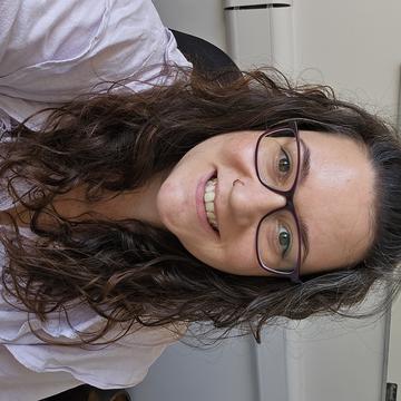 Hannah has long dark wavy hair wearing, glasses and smiling.