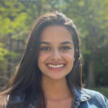 A headshot of Deanna Giraldi, with long dark shoulder-length hair, shows her smiling while wearing a denim jacket and looking directly at the camera.