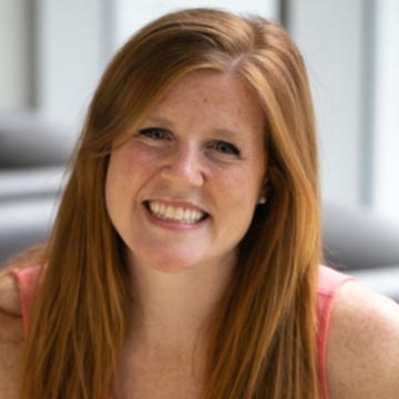 Kathleen is smiling  at the camera with long red hair smiling wearing a peach coloured top.