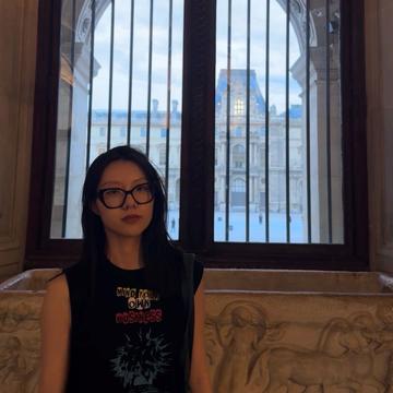 Wange Li is standing in a traditional building, wearing a black top with shoulder length hair, looking at the camera.