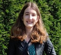 Chloe Brimicomb has shoulder-length brown hair and is wearing a blue jacket, standing in front of a green background