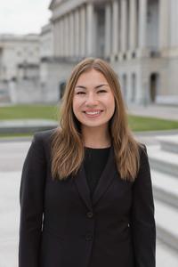 Miya Rosenthal is smiling in front of a set of steps, wearing a black blazer. She has shoulder-length light brown hair.