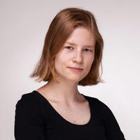 Sara Hueber has bobbed hair and is wearing a black top. She is in front of a plain background.