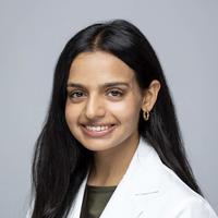kapoor nandini wears a lab coat, has long dark hair and is smiling in front of a plain background