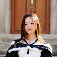 Vivian Gu wears academic dress, has long dark hair and stands in front of a set of steps
