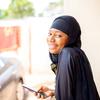 A young smiling Nigerian woman looking at the camera, holding a mobile phone