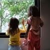 Two young children seen from behind. They are standing and looking out of a large window at some trees. -- Odua Images, stock.adobe.com
