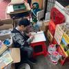 Chinese child does homework inbetween boxes of store supplies