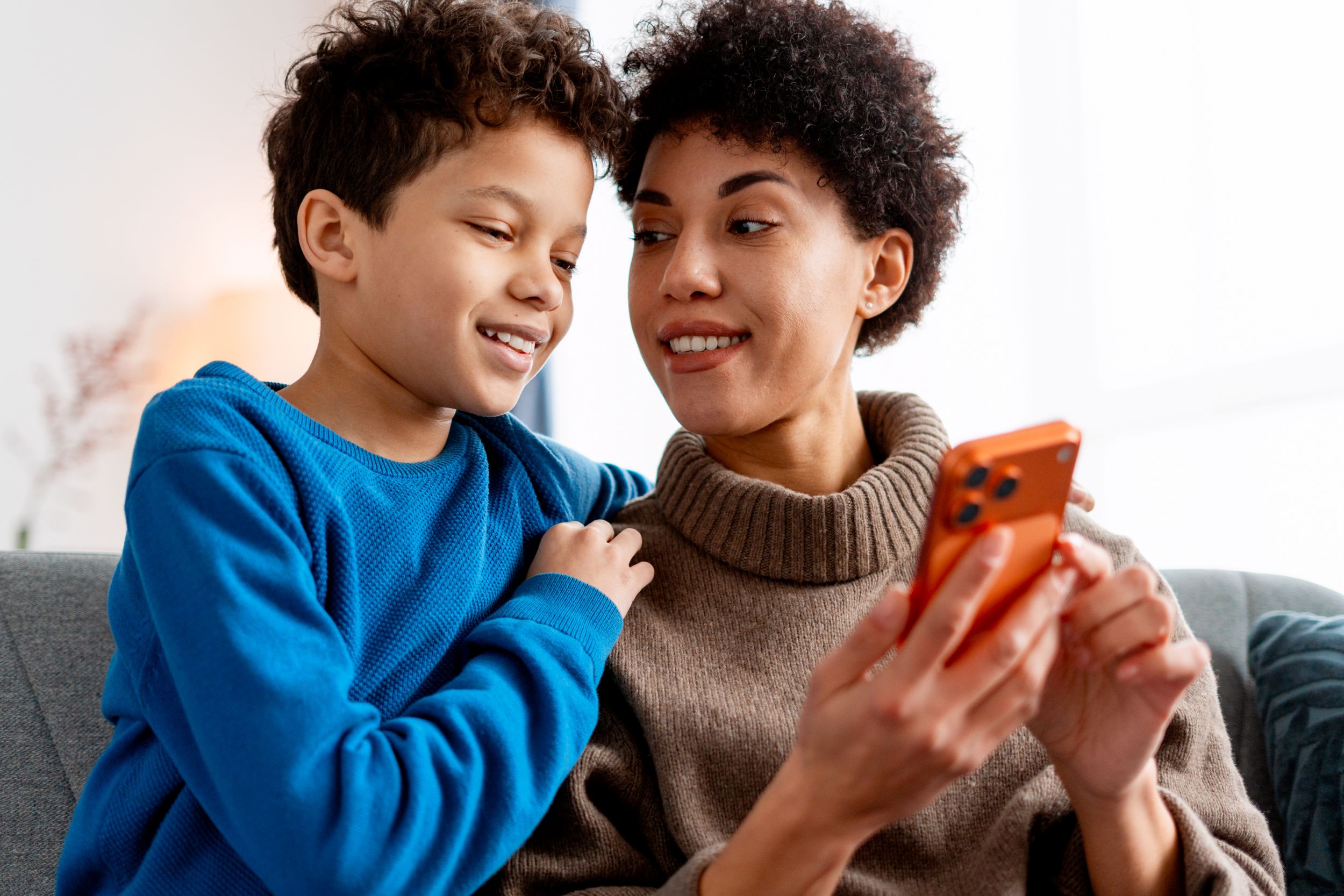 A mother and child sitting on a sofa, looking together at a phone
