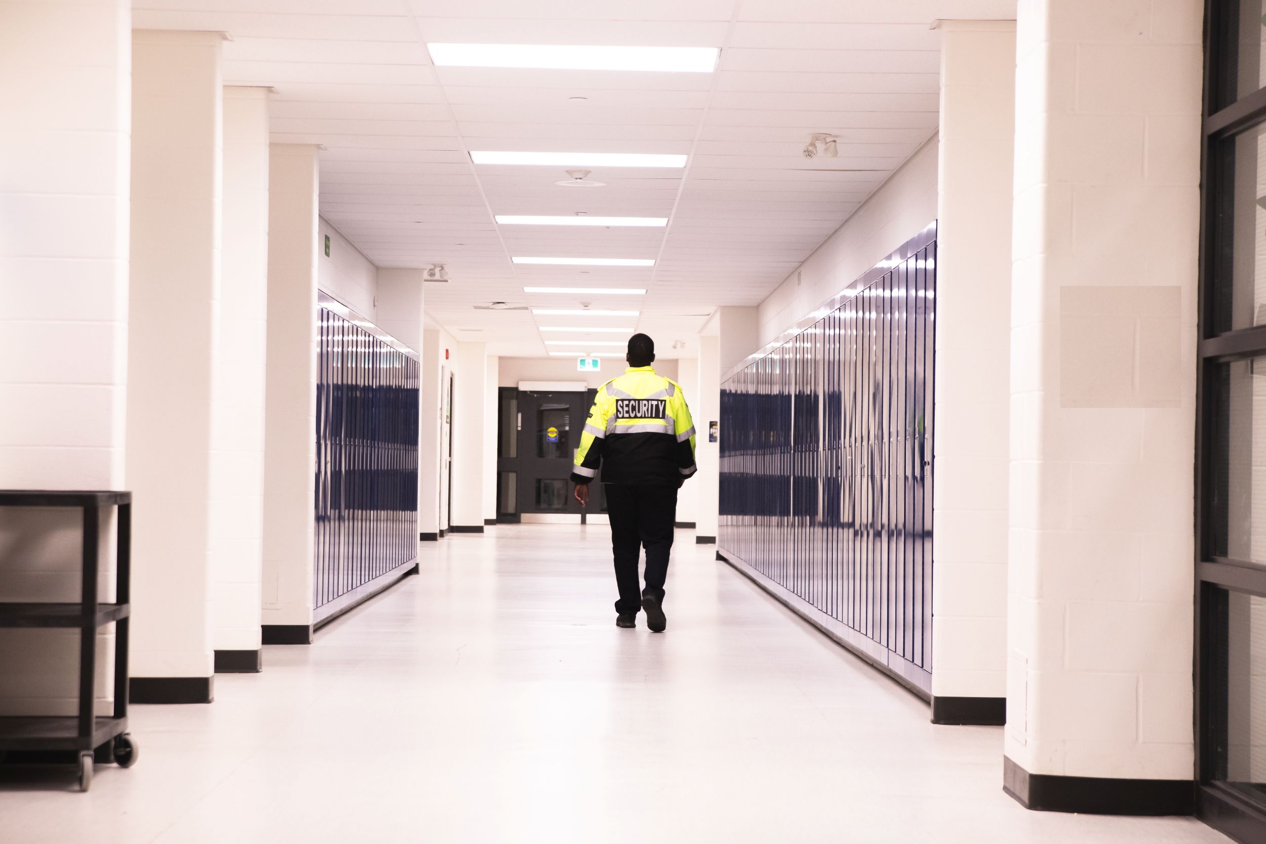 A security guard walks along a long school corridor lined by lockers