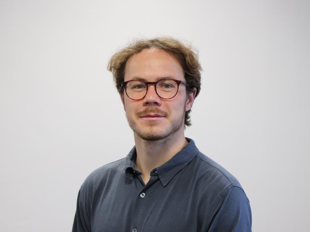 William Rudgard has short brown hair, is wearing glasses and a navy blue shirt