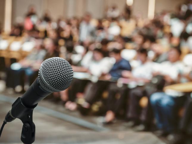 A close up of a microphone, in front of a large seated audience. Credit:&nbsp;Tzido&nbsp;- Getty Images-829570660