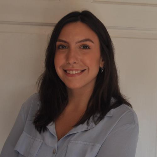 Luciana Leite has long dark hair and is wearing a light blue blouse. She is smiling at the camera.