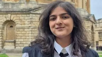 Shrutika Jha standing in front of the Bodleian Library. She has long wavy black hair and is in academic dress